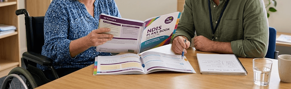 A support participant and a CDC team member sitting together at a table, going through an NDIS plan booklet page by page.